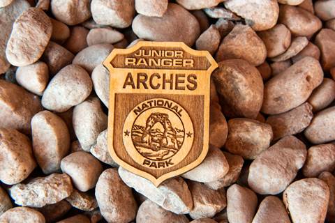 wooden badge with the words "Junior Ranger Arches" and a drawing of a stone arch