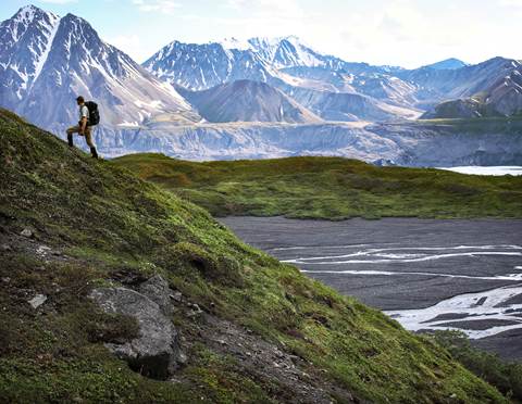 A man hiking up a hillside in front of a vista of mountains and rivers