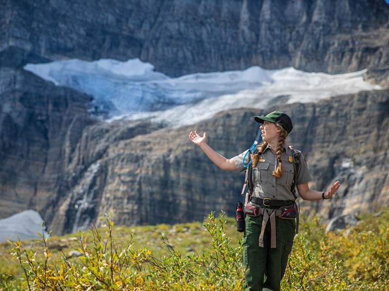A park ranger standing with arms out in front of snow and ice.
