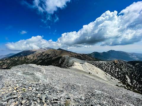 a bare alpine ridge with blue sky and white puffy clouds above.