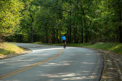 A lone bicycle rider wearing a blue jersey rides up an open mountain road.