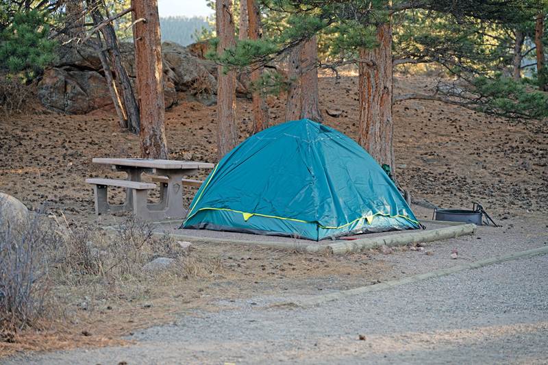 A green tent is set up on a tent pad in a campsite