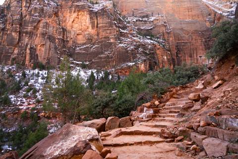 A set of red sandstone stairs lined with loose rocks and green foliage leads out of frame.